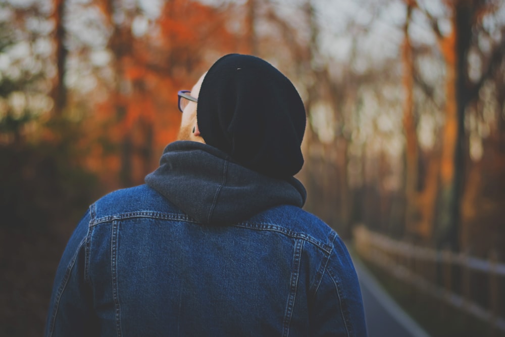 person in blue chambray hoodie walking on walkway between trees