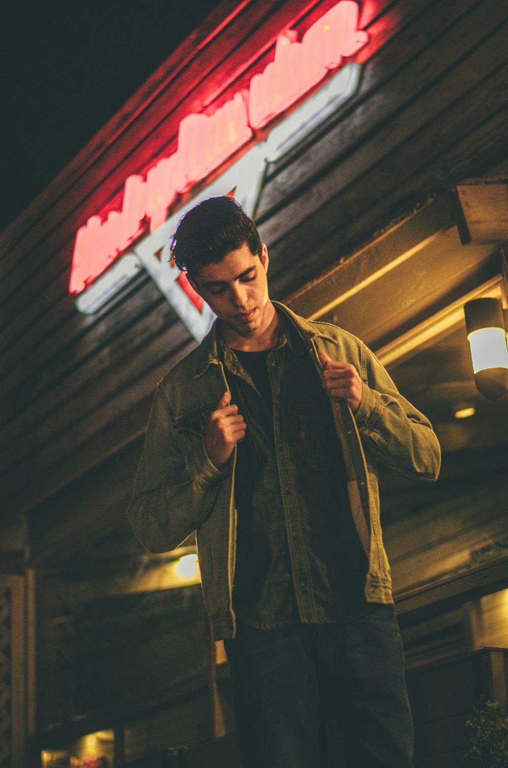 man holding his brown jacket and standing in front of brown concrete storefront low-angle photo