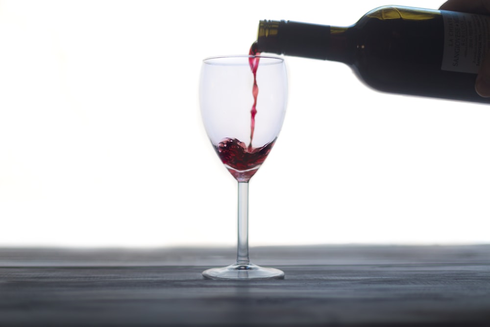 bottiglia di vino che versa su un bicchiere di vino trasparente