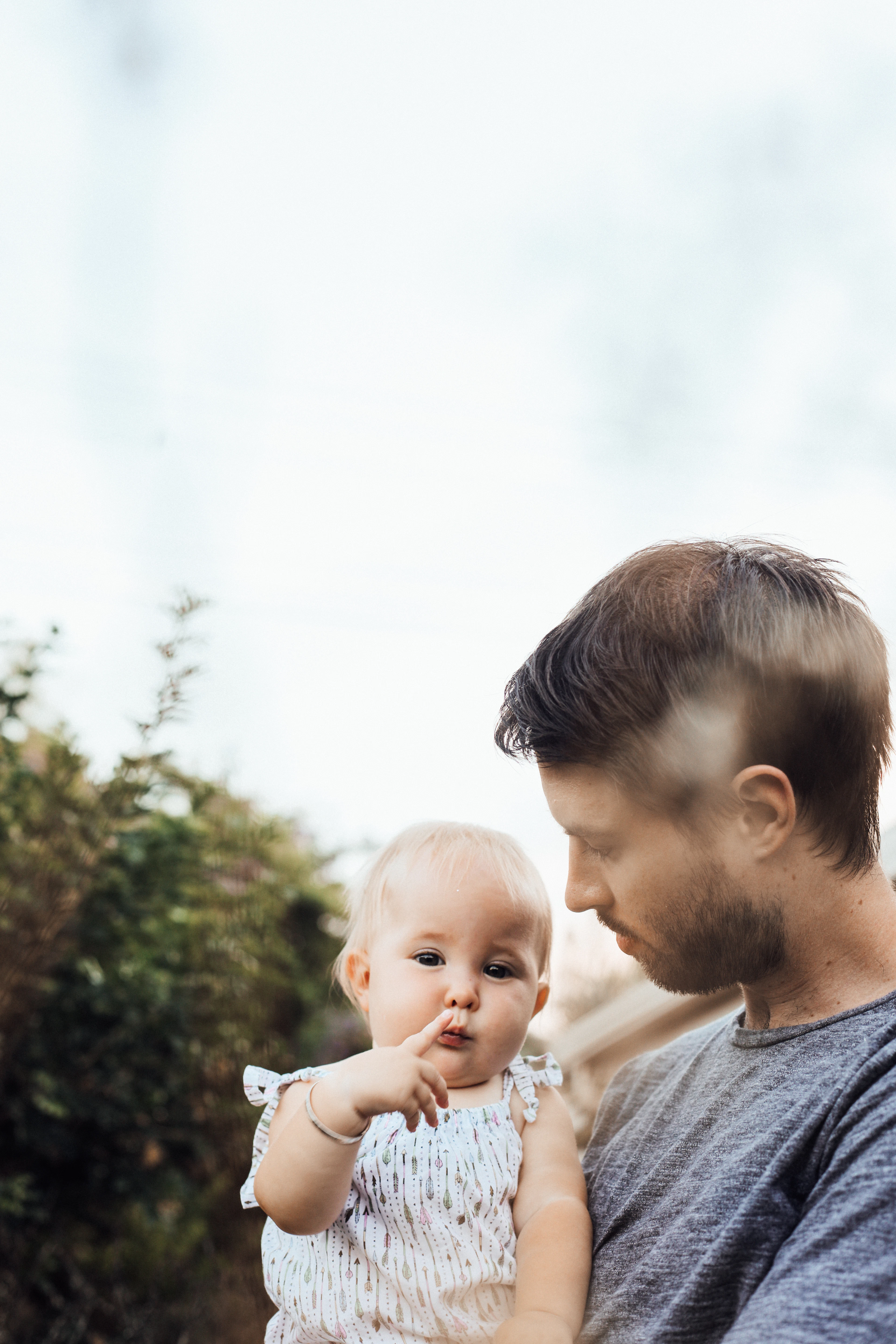 Man in grey holding a baby outdoors in soft light