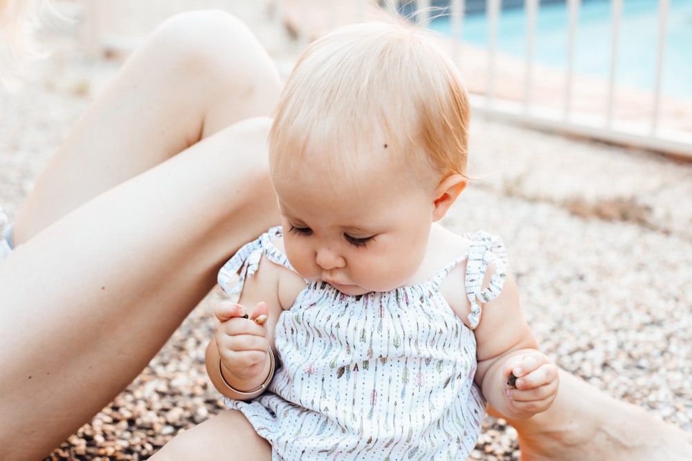 baby sitting on sandy ground while holding pebbles