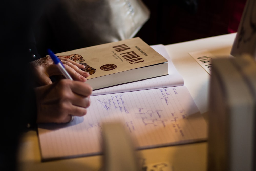 Persona escribiendo en cuaderno cerca del libro