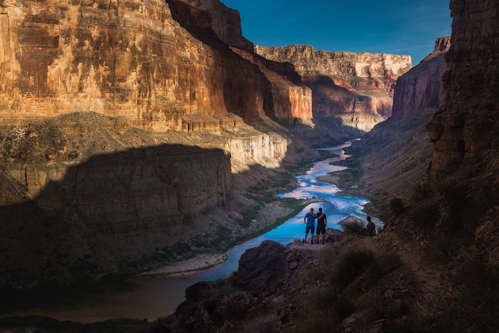 two person standing on rocks facing body of water