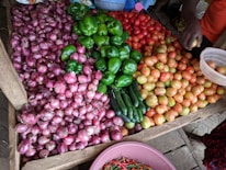 Close-up of hands selecting fresh onions and tomatoes at a market stall.