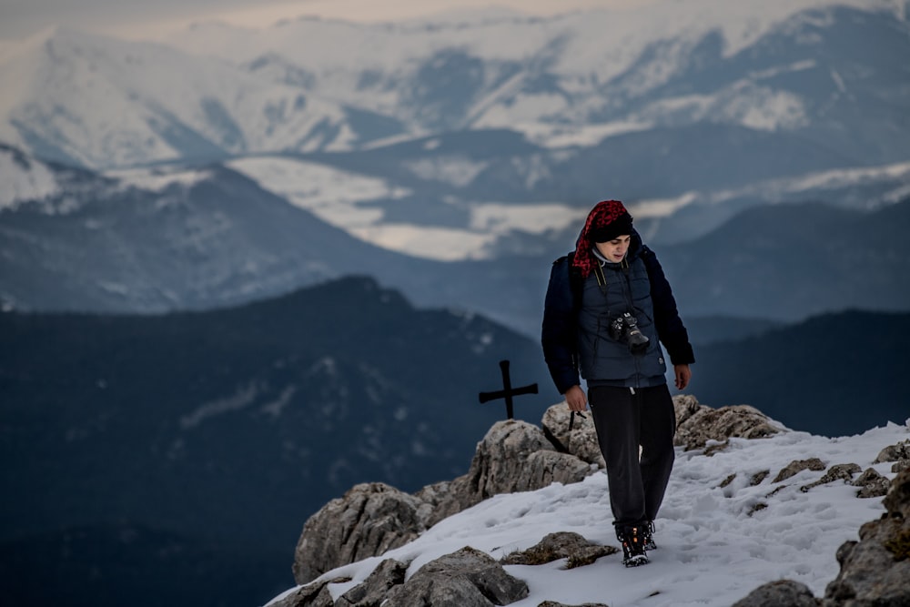 man standing on peak near cross at daytime