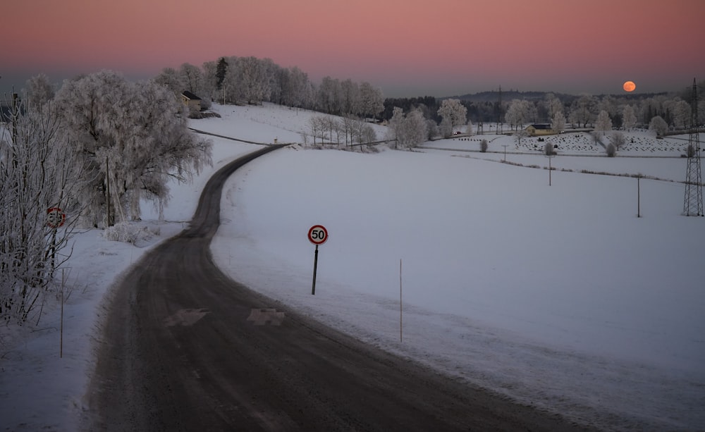 Graue Asphaltstraße zwischen weißem Schneefeld bei Sonnenuntergang