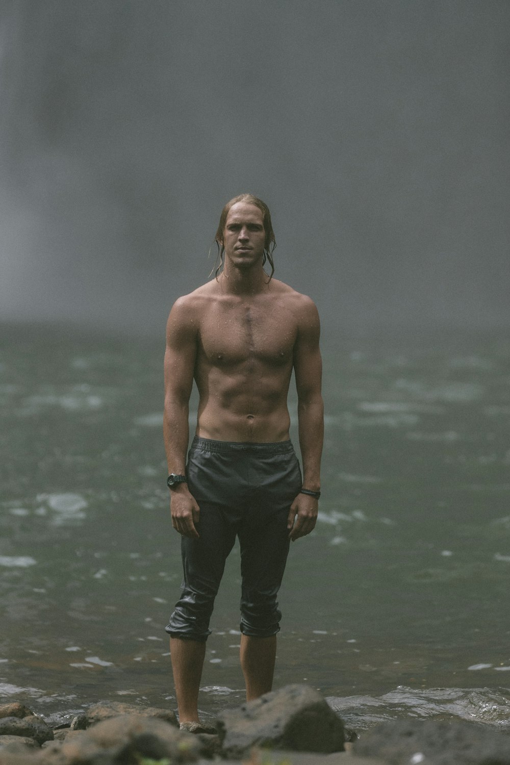 man wears black pants stands on rocks near body of water