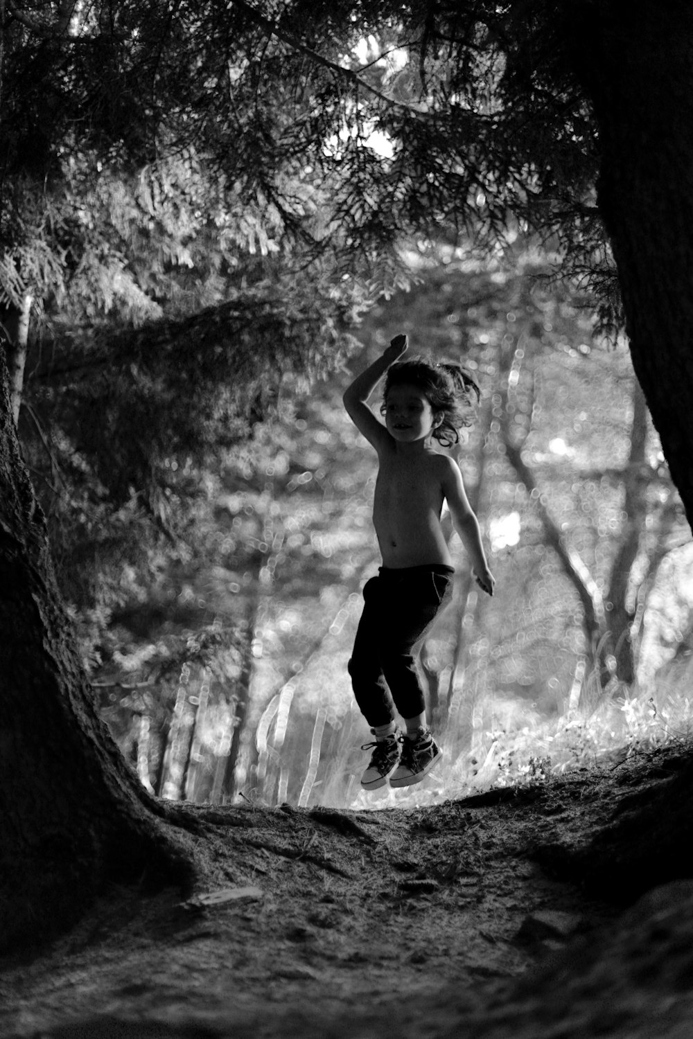 Foto en escala de grises de un niño saltando cerca de los árboles