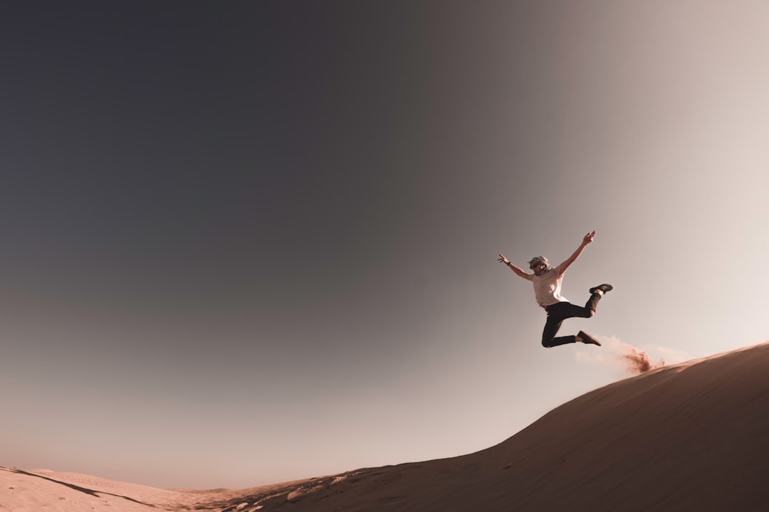 person jumping from sand dune during daytime