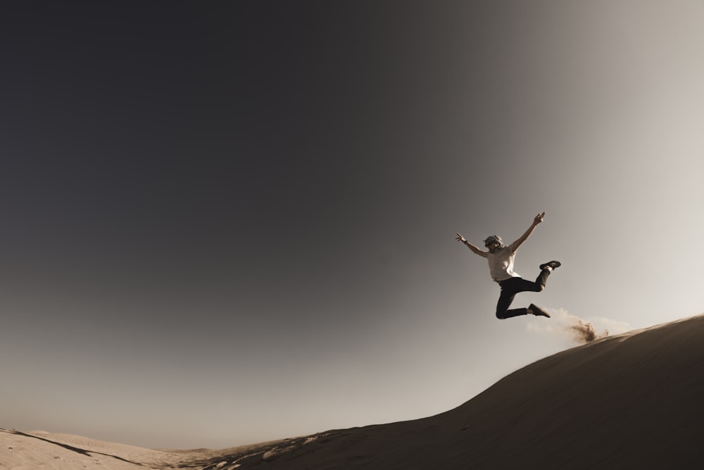 person jumping from sand dune during daytime