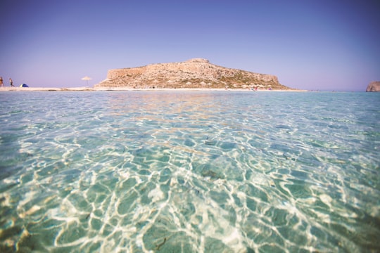 people walking near brown hill surrounded by body of water during daytime in Chania Greece