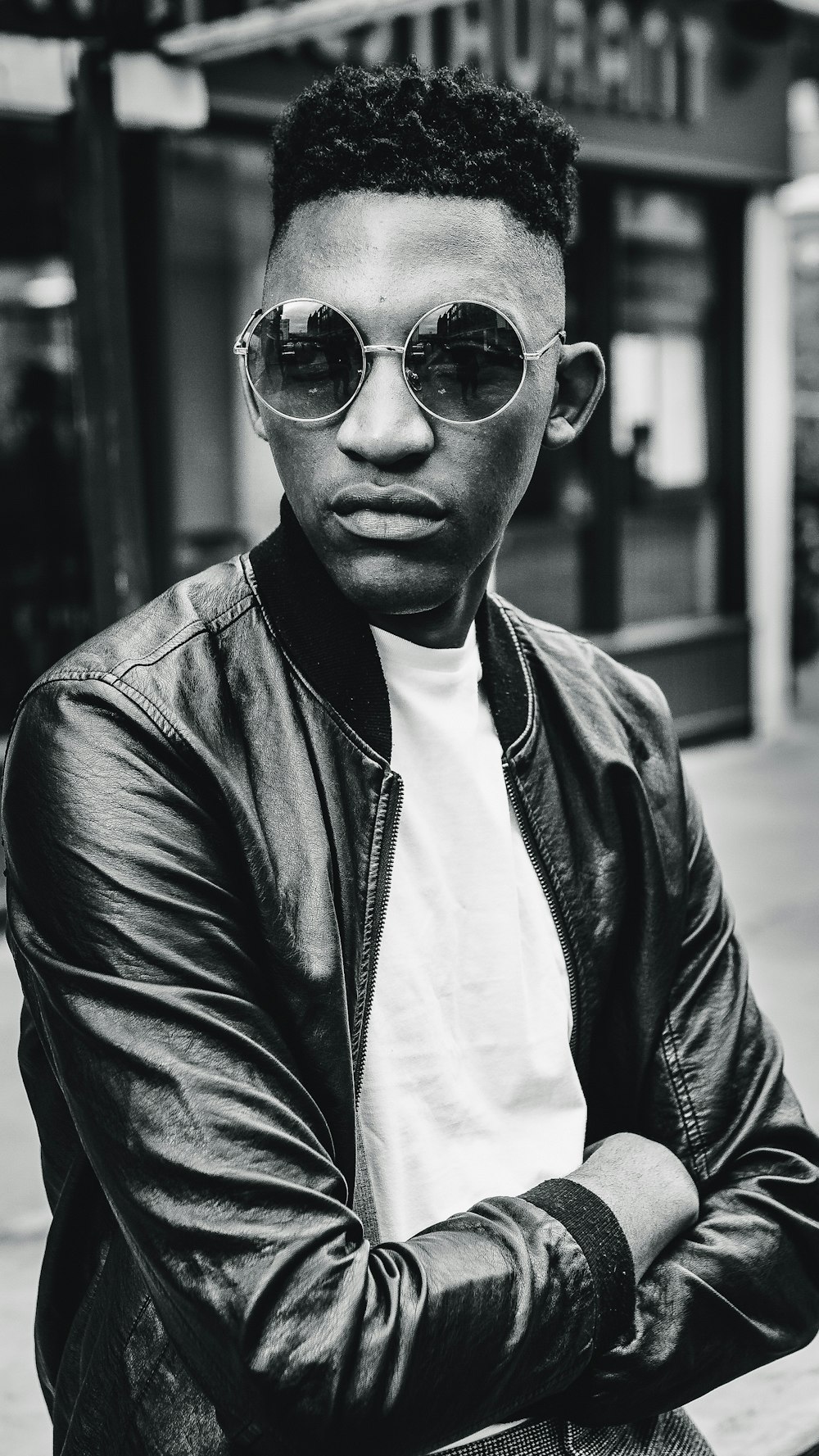 grayscale photo of man wearing bomber jacket standing outdoor during daytime