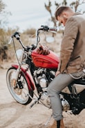 man sits on red and black Harley-Davidson motorcycle during daytime