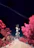 A telecommunications tower is positioned at the center of a rocky pathway, surrounded by vibrant, surreal pink foliage and a deep blue sky. A distinct contrail stretches diagonally across the sky, adding to the otherworldly atmosphere.
