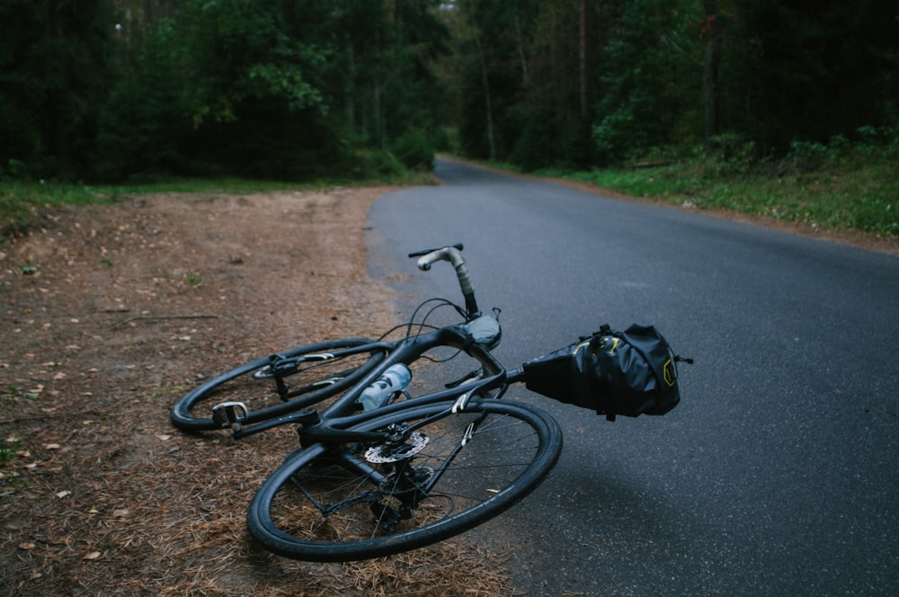bicicleta de estrada preta deitada na estrada de asfalto durante o dia