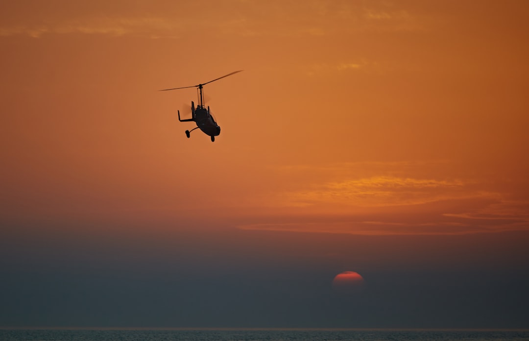 silhouette of helicopter flying during sunset
