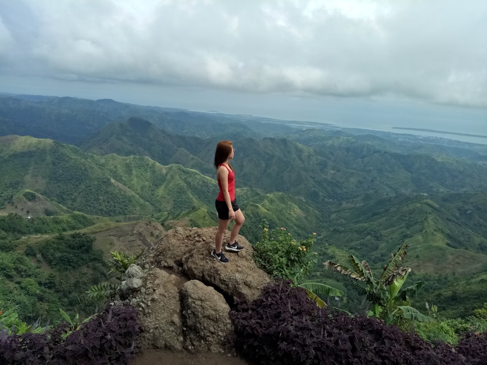 woman in red tank top standing on rock formation during daytime