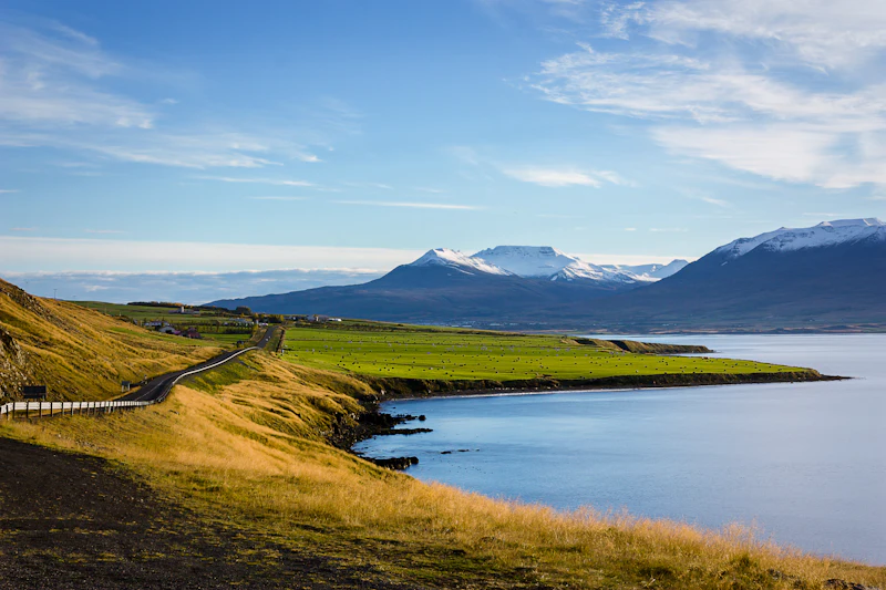 Open field and low mountains beside still water in soft pale light