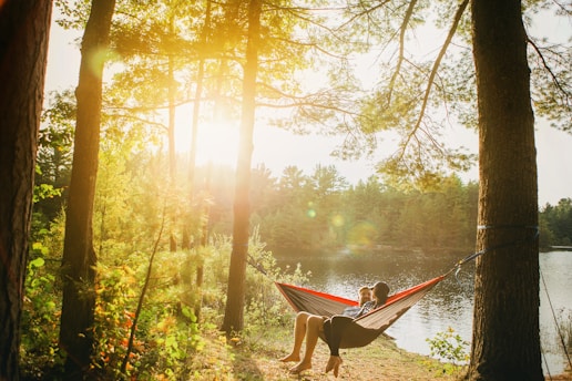 man and woman seating on gray hammock beside trees during daytime