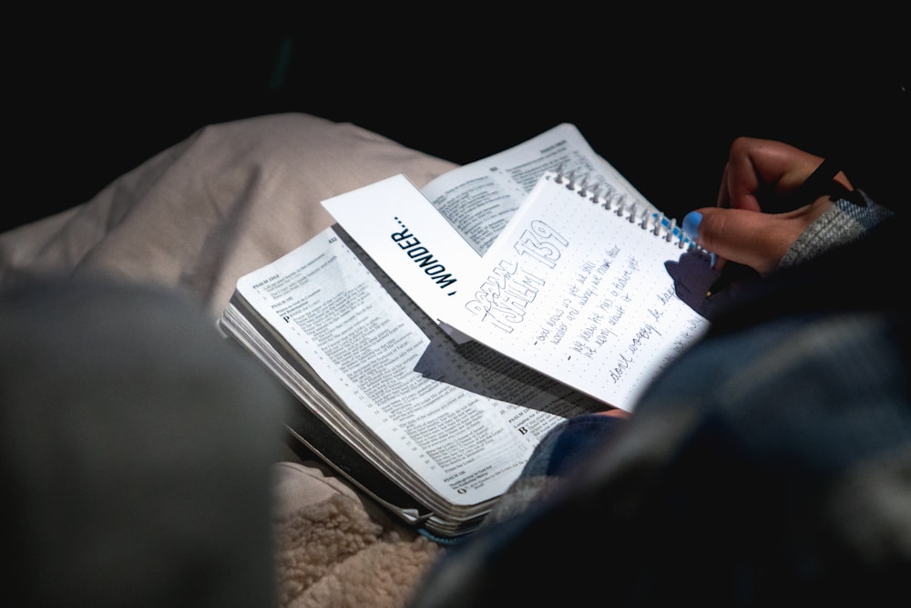 Persona que sostiene un bolígrafo negro y escribe en un cuaderno blanco