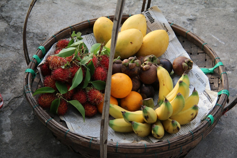 canasta de plátanos amarillos, mangos amarillos, rambután rojo, naranjas y mangostán