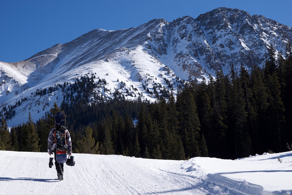 person walking on snow road facing mountain at daytime