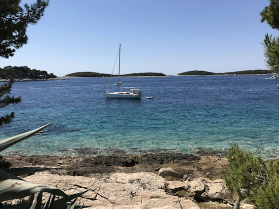 A serene coastal view of the Aeolian Islands with a small sailboat gliding near rocky shores under a clear blue sky.