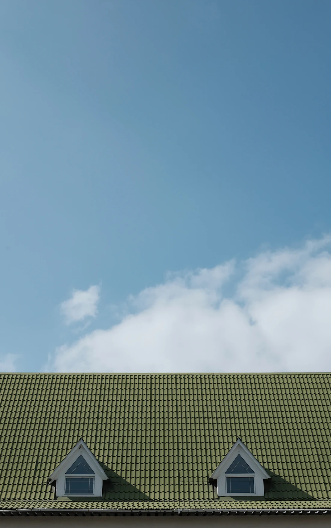 A pitched tiled roof with dormer windows against a blue sky