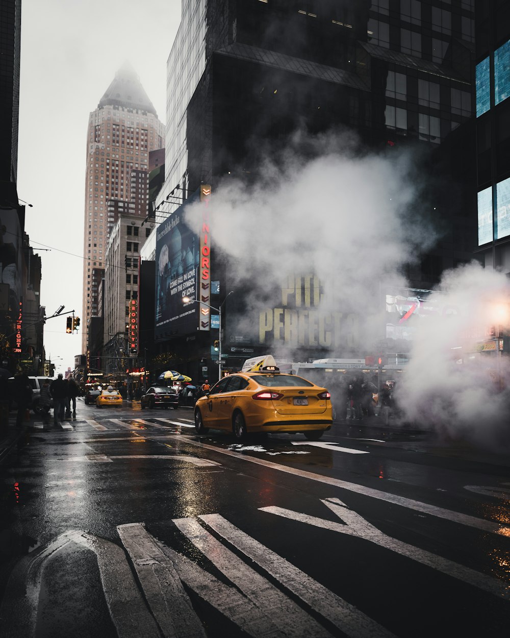 yellow taxi sedan on gray concrete street passed through white smokes near walking lane