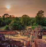 Sunset casting golden light over ancient ruins nestled in lush greenery.