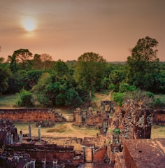 A serene mountain landscape with ancient ruins nestled among lush greenery under a golden sunset.