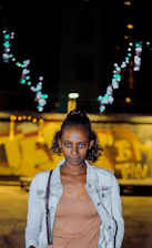 Close-up of a model wearing a graffiti-inspired jacket under city lights at dusk.
