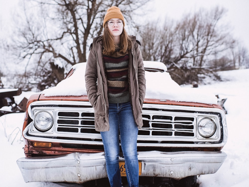 Mujer apoyada en un coche cubierto de nieve