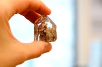 Close-up of hands holding a crystal with soft ocean waves blurred in the background.