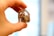 A hand holds a clear, faceted crystal with brown inclusions. The background is softly blurred, highlighting the delicate details of the crystal's inner textures.