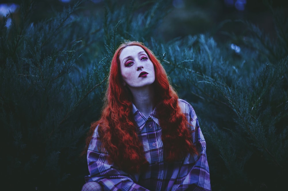 photography of red-haired woman standing near leafed plants