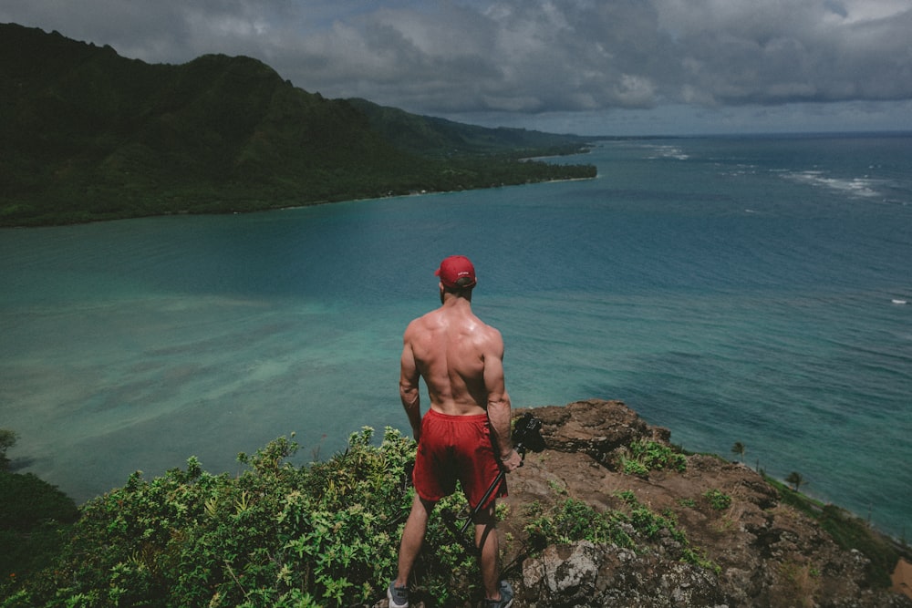 man standing on top of clipp watching body of water during daytime