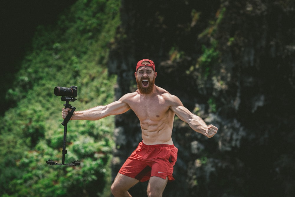 standing man wearing red shorts and holding black camera