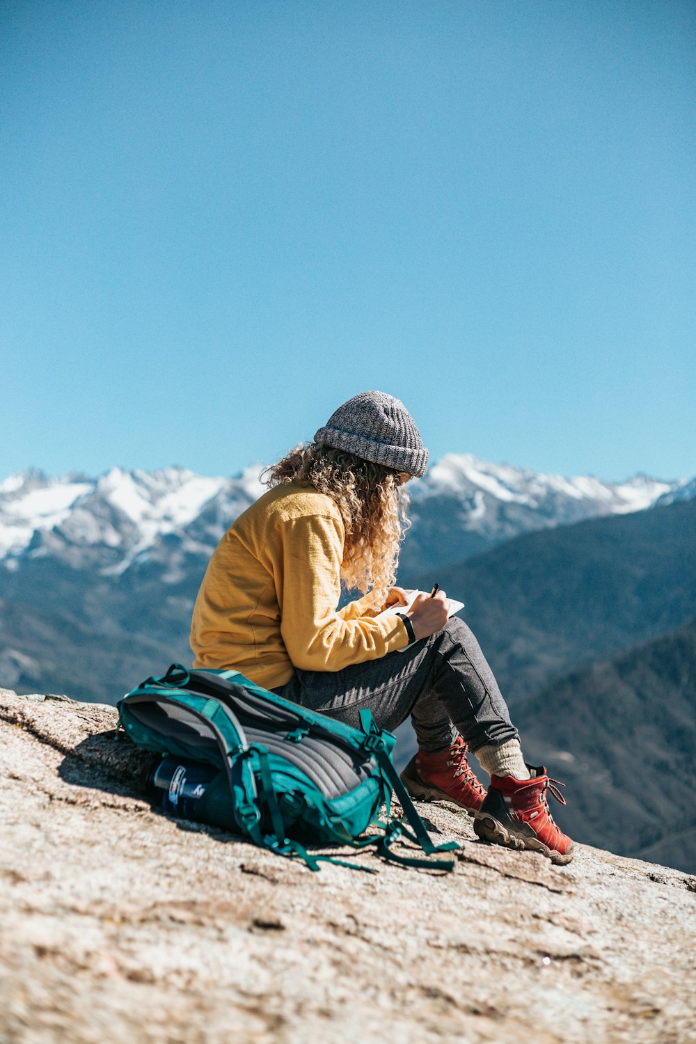 woman writing while sitting on hill near mountain