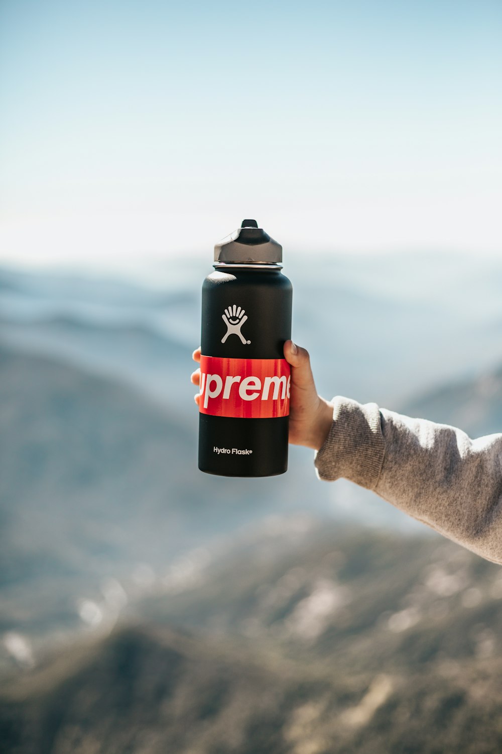 person holding black and red Supreme sports bottle