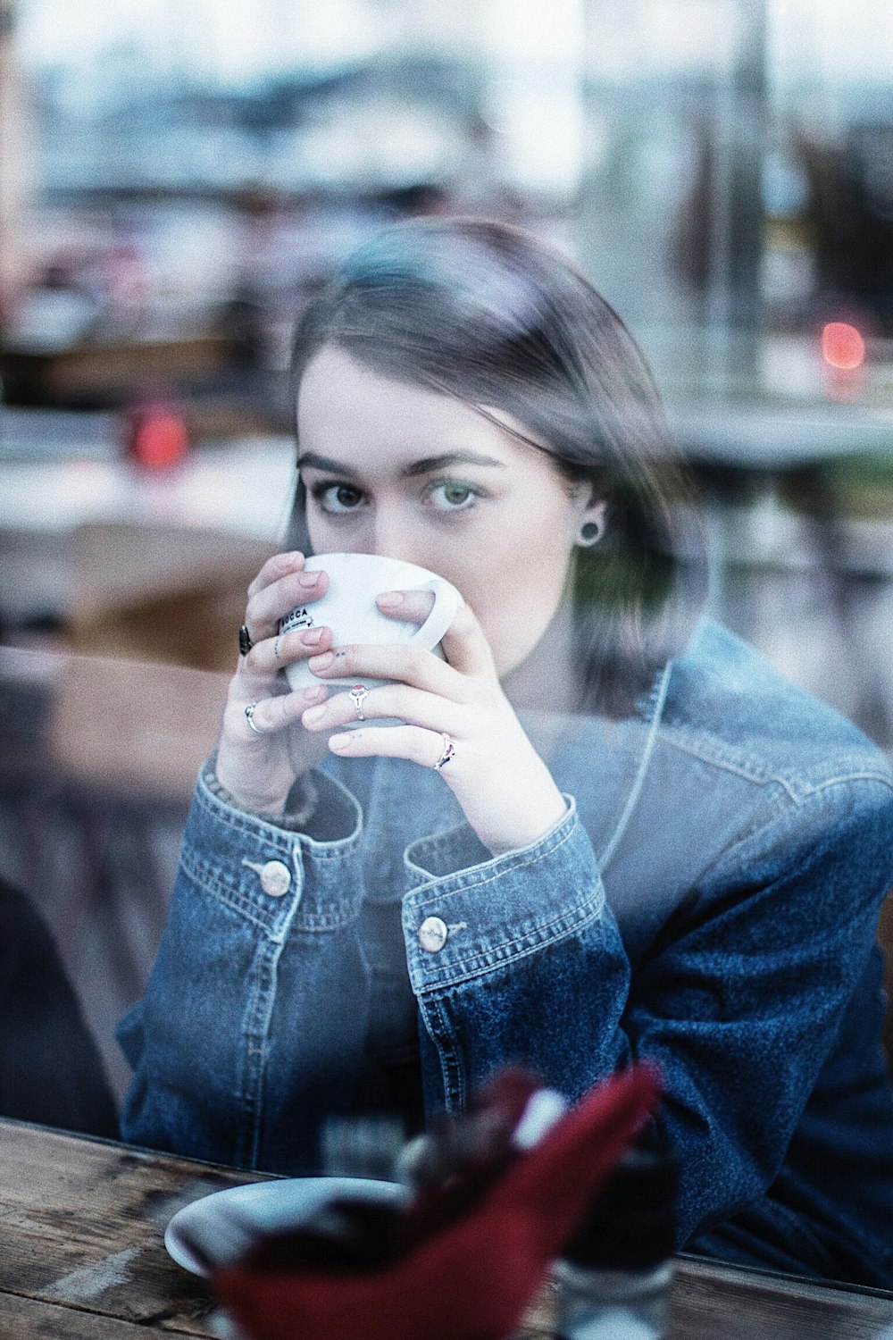 donna che indossa una giacca di jeans blu che tiene una tazza da tè in ceramica bianca
