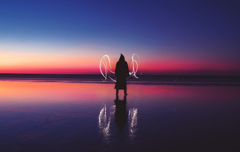 silhouette of person standing on body of water with light wave