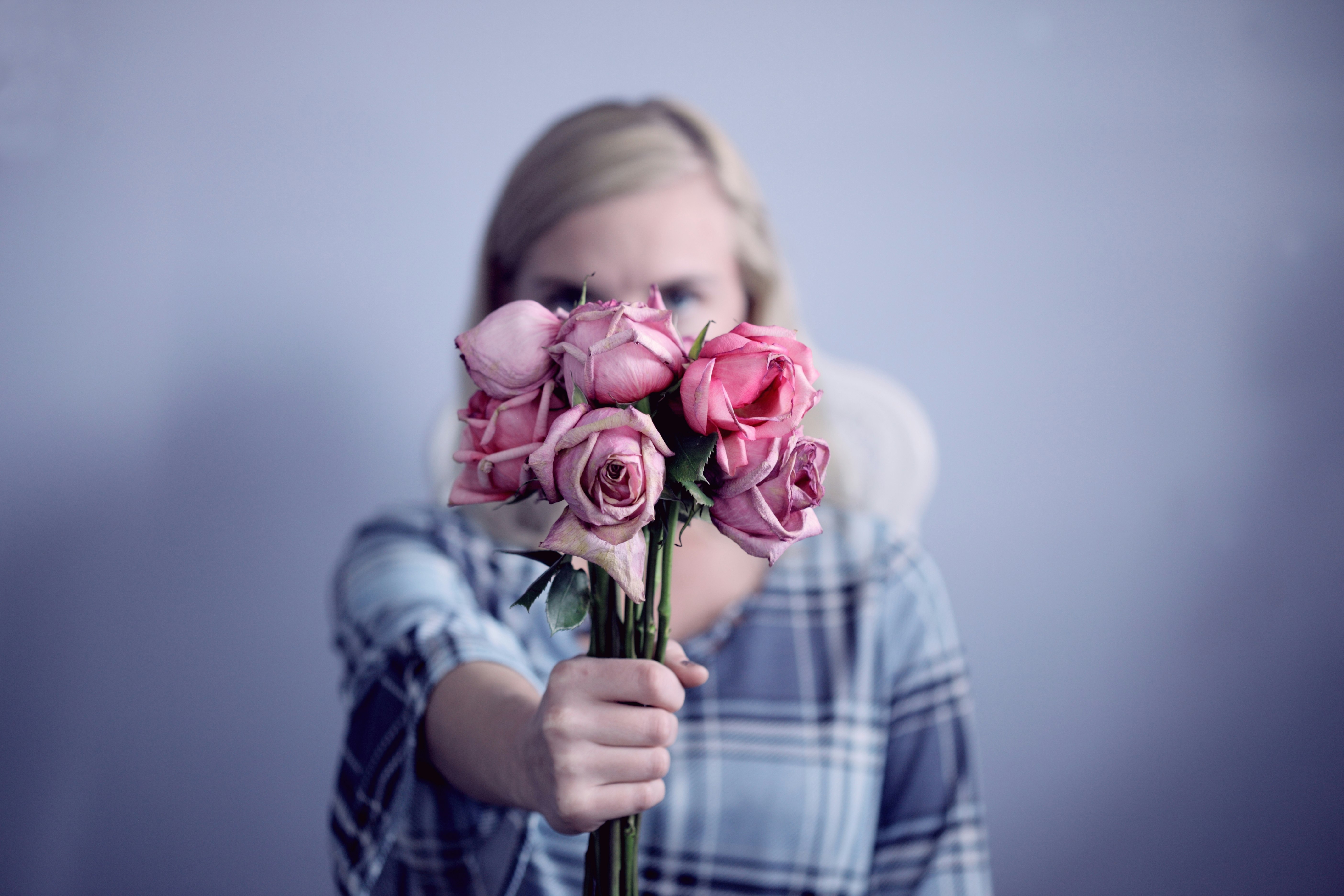 A young woman holding a sad bouquet of dying roses.