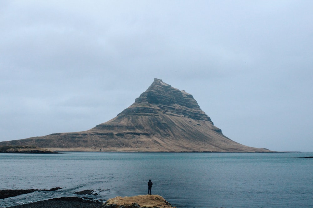 man standing in front of body of water near island