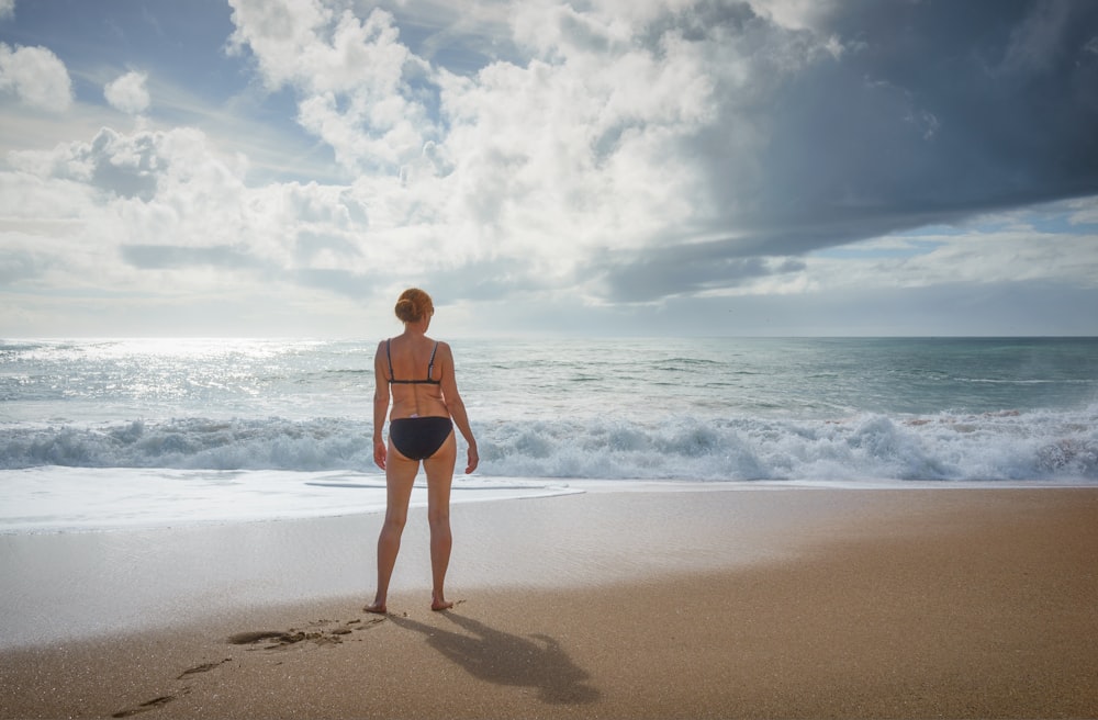 mulher em pé na costa de frente para o oceano