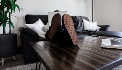 person sitting on sofa resting its feet on top of coffee table while using laptop comfortable zoom background