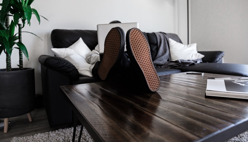 person sitting on sofa resting its feet on top of coffee table while using laptop