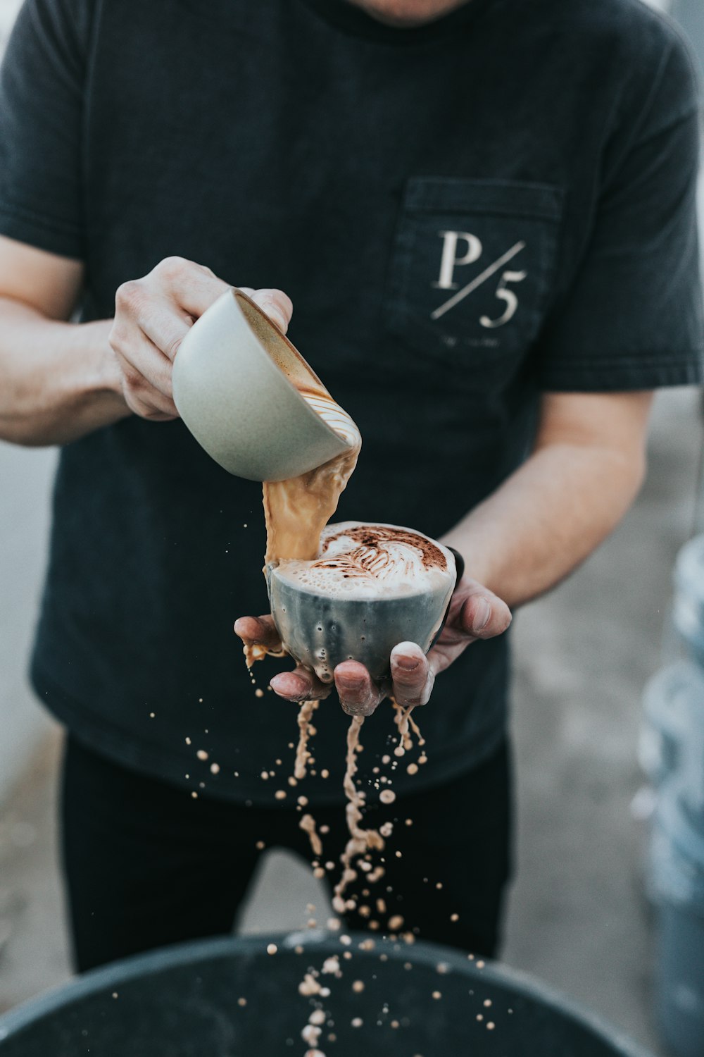 man holding two gray ceramic teacup pouring the other one