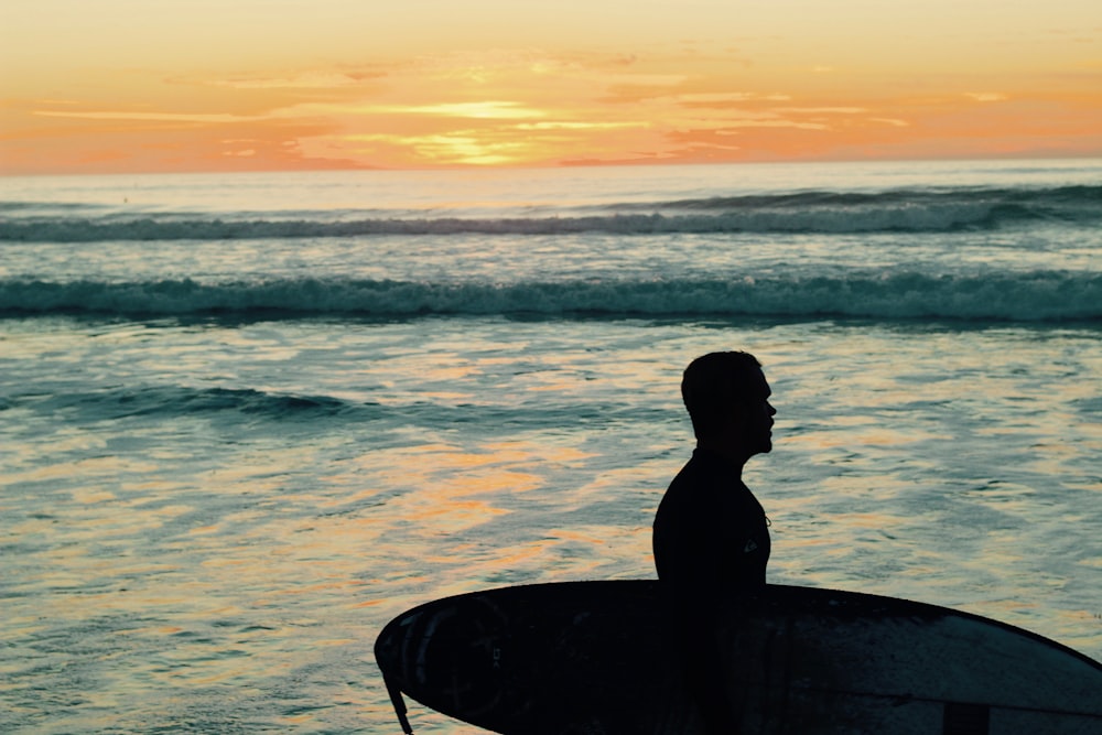 silhouette photo of man holding surfboard