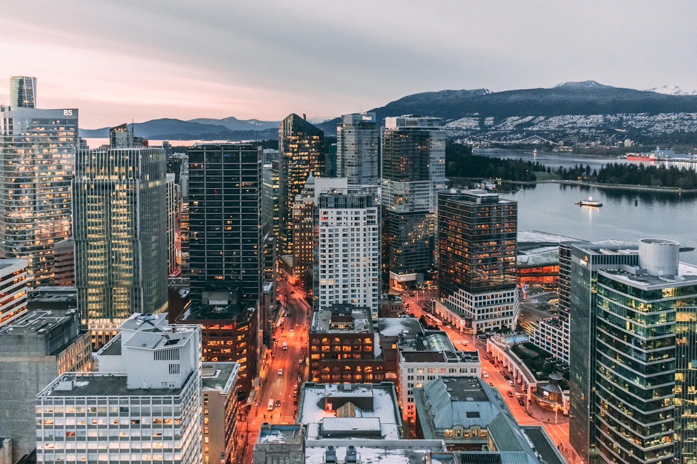 Aerial view of downtown Vancouver British Columbia at dusk with the harbour and the snow-dusted North Shore mountains behind the lit skyline